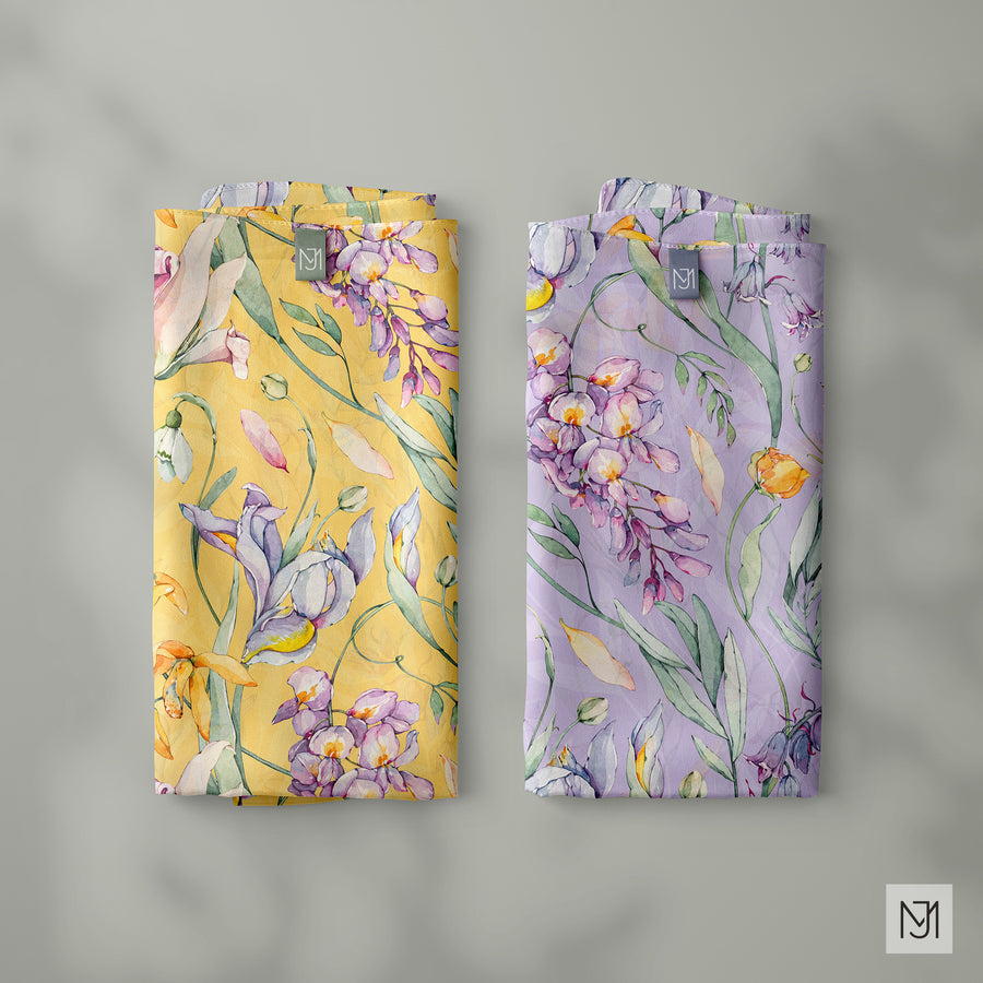 The Botanical pattern by Media Jamshidi, shown on two folded silk scarves, one in yellow and one in lavender, both with the same mixed spring flowers.