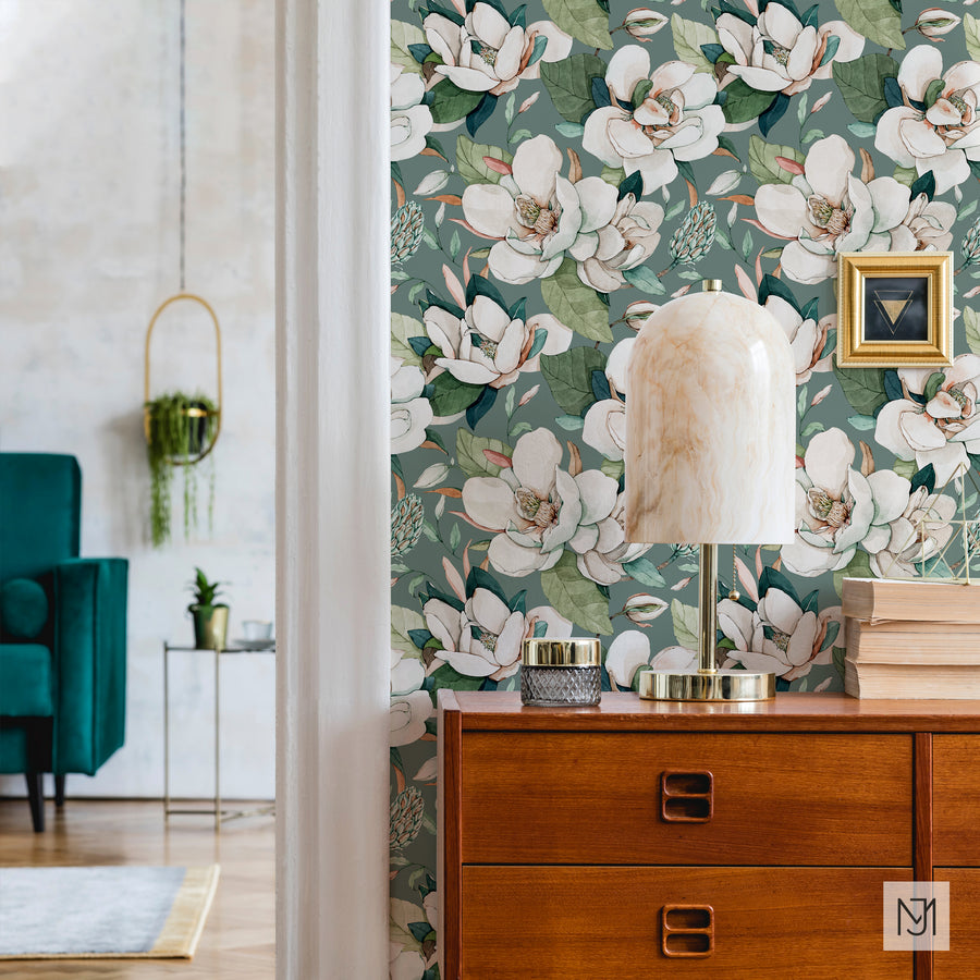 White Magnolia pattern as wallpaper behind a wood dresser, with a marble table lamp, a stack of books, and a small framed art print.