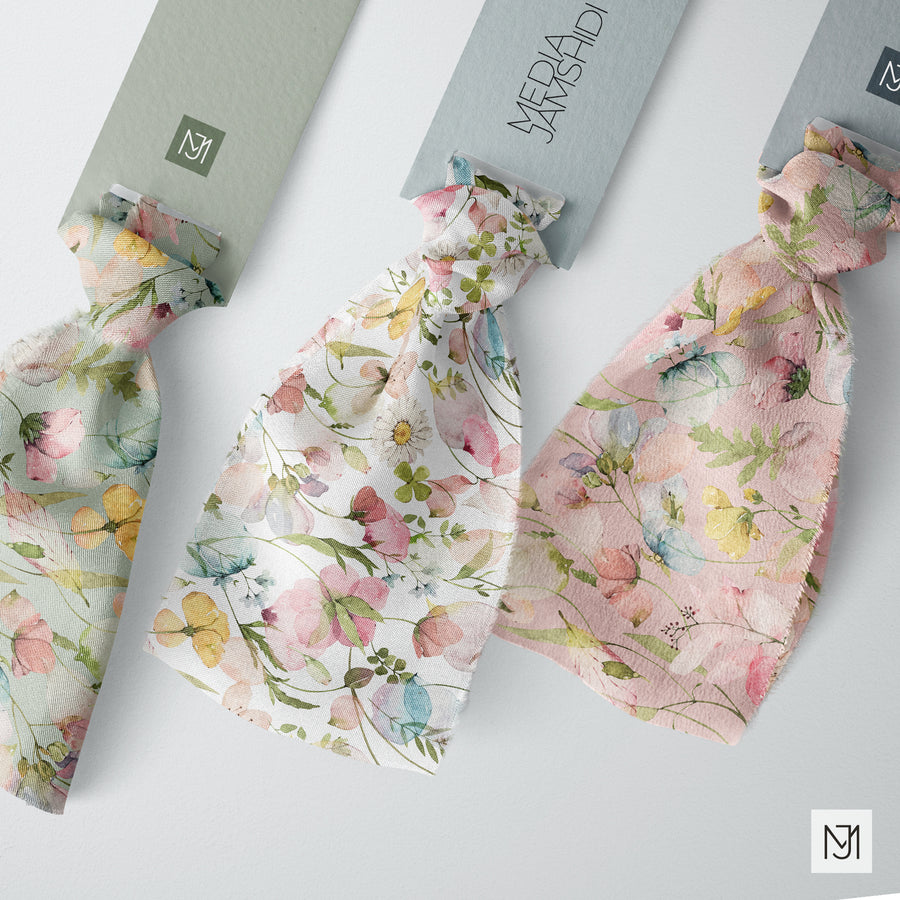 Three knotted fabric ribbons of the Botanical pattern in sage green, white, and blush pink colorways, each with a small brand tag.