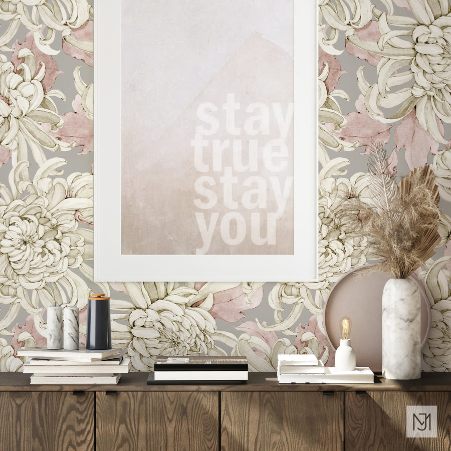 The Chrysanthemum pattern by Media Jamshidi, as a wallpaper mural in a dusty pink and gray colorway, behind framed art and a marble vase with dried pampas grass.