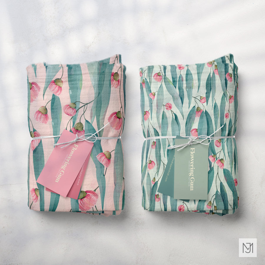Two folded fabrics of the Australian Flowering Gum pattern, one in a blush pink colorway and one in sage green, each with a small brand tag.