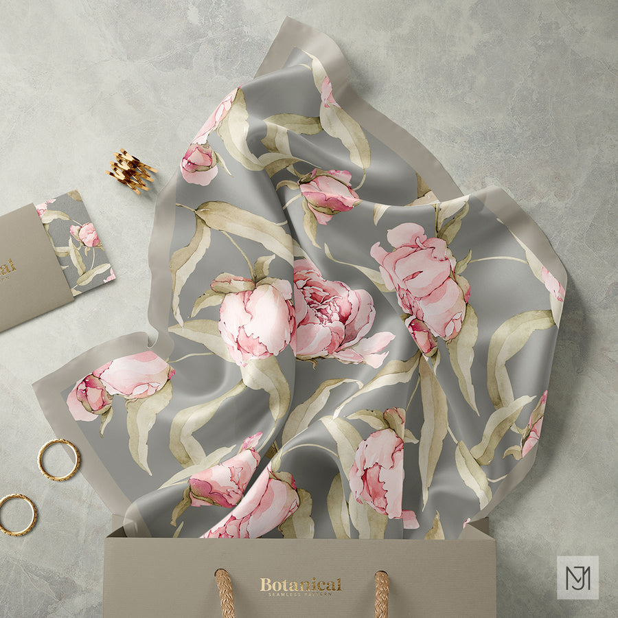 The Peonies pattern on a silk scarf and a small notecard, styled with a gift bag and gold jewelry on a marble surface.