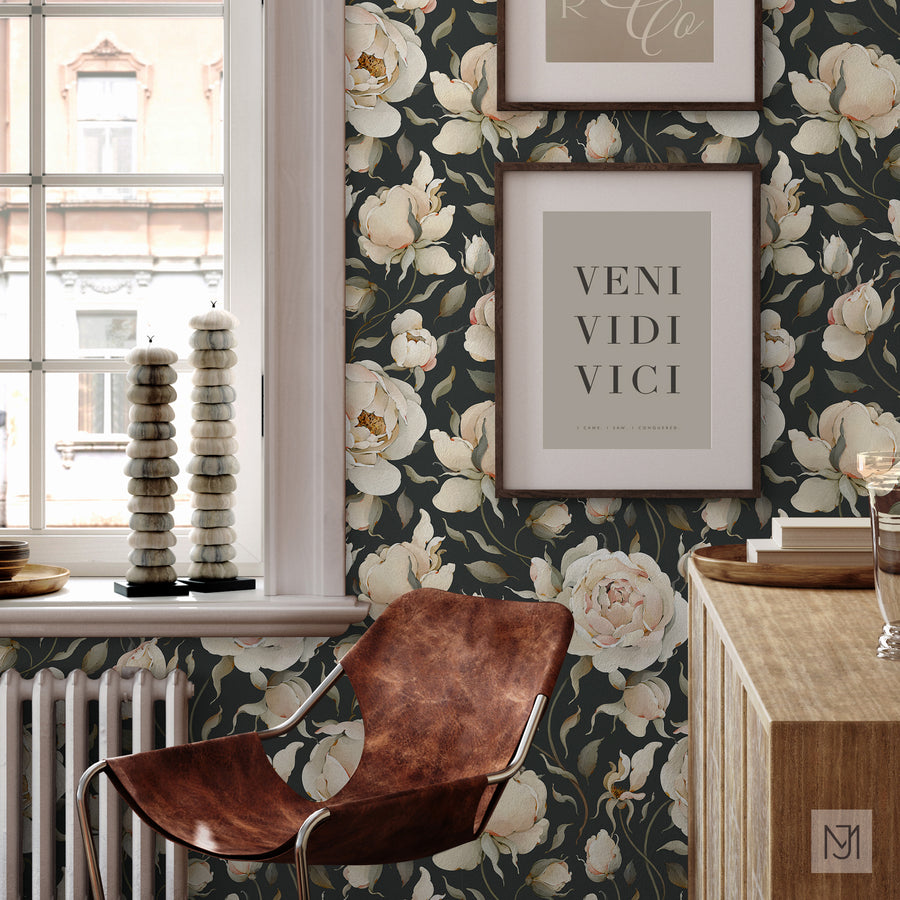 Roses pattern as wallpaper in a dark charcoal colorway, behind framed art prints, a leather chair, and a wood console table.