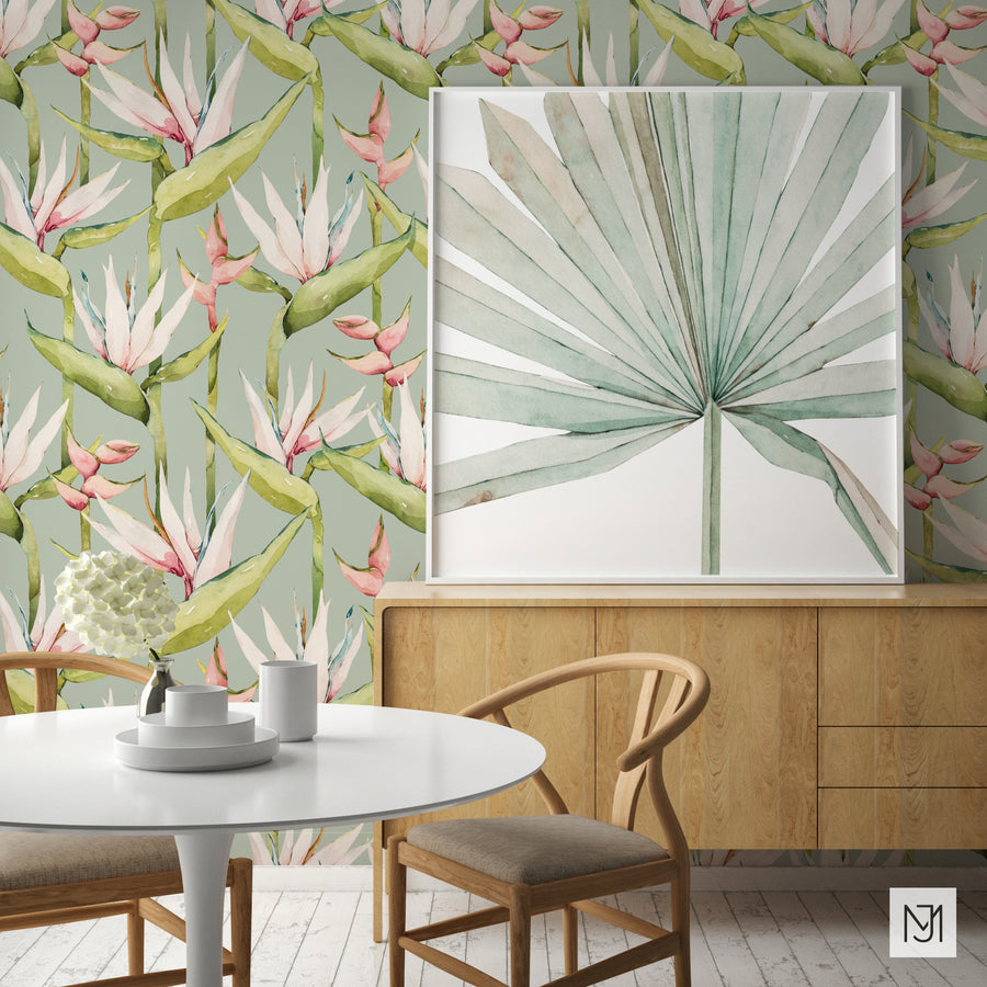 Tropical pattern as a wallpaper mural in sage green, with a framed botanical leaf print, wood sideboard, and dining table with wishbone chairs.