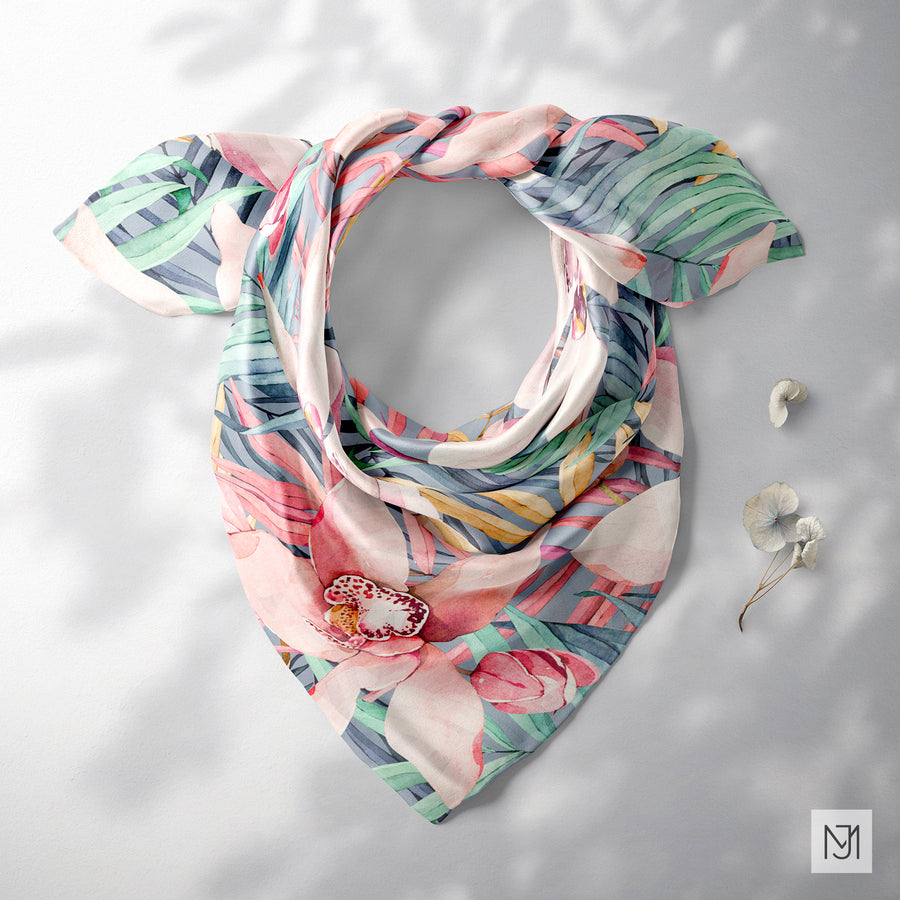 Tropical pattern printed on a silk scarf, tied in a loose knot, in a blue-gray colorway with the same pink blooms and leaves.