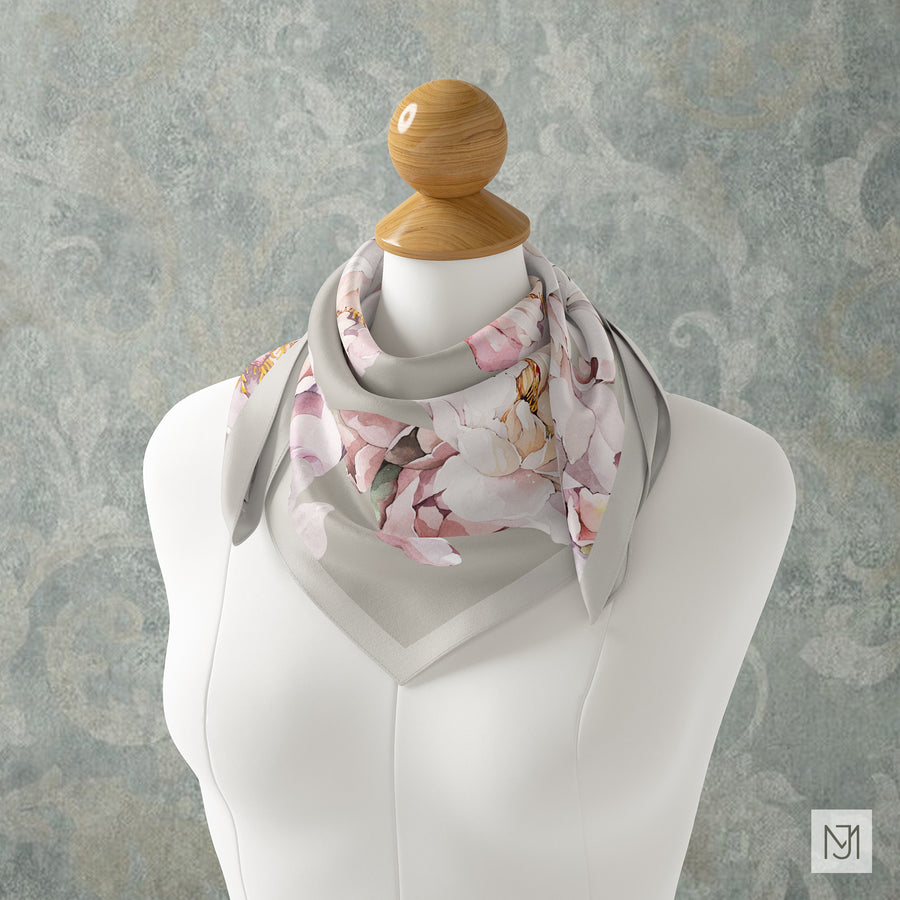 The White Peony pattern on a silk scarf tied at the neck, in a dusty rose and gray colorway, against a teal-gray backdrop.