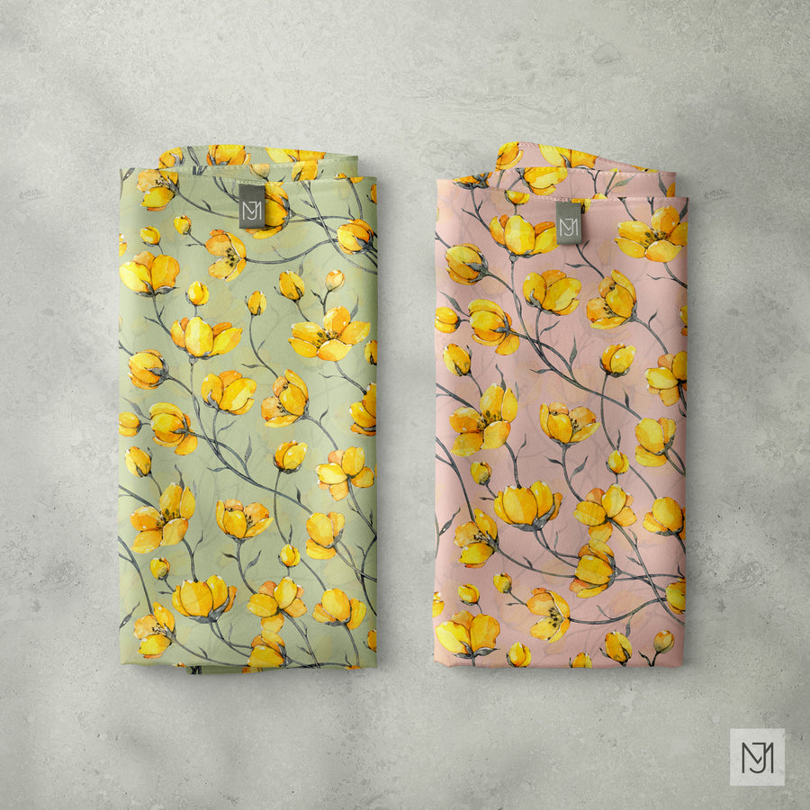 Two folded fabrics of the Yellow Garden pattern, one in sage green and one in blush pink, each with a small brand tag.
